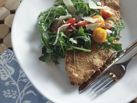 baked chicken cutlets topped with arugula, tomato, and onion salad