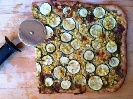 pizza topped with spicy pesto, fresh corn kernels, and thinly sliced zucchini